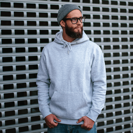 Man stood face on showing off a grey hoodie he has designed. 