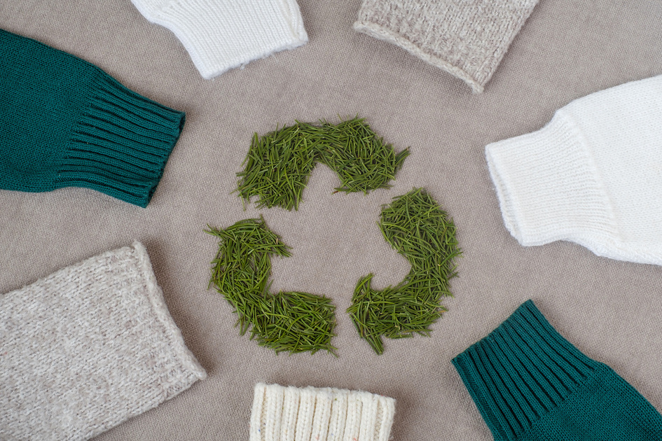 Recycling symbol made from green material, surrounded by six jumpers made from sustainable materials.