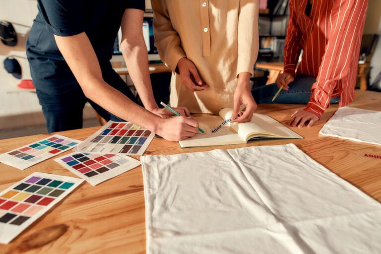 Three people showing the process of positioning designs for your own clothing brand.