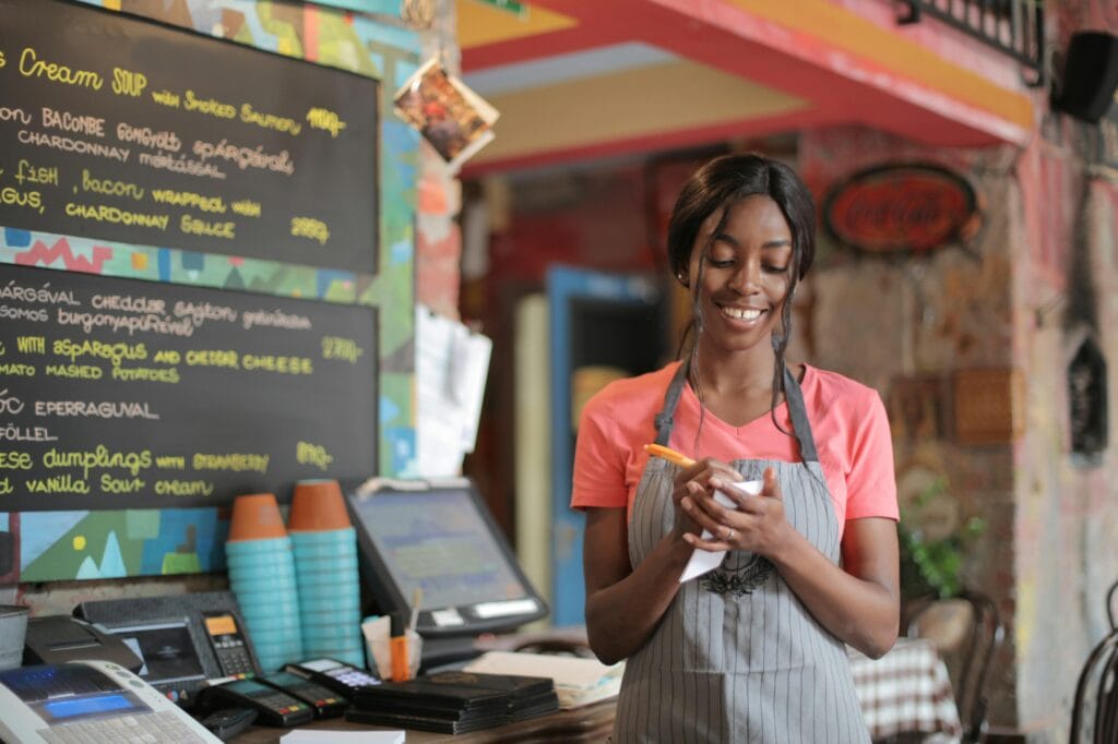 A waitress wearing a grey pinstripe apron and bright pink t-shirt as part of her restaurant uniform. 