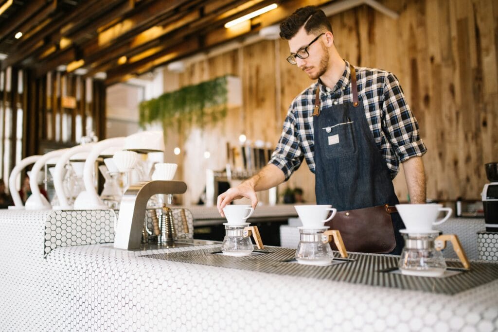 Barista wearing a chequered shirt serving coffee at a bar. 