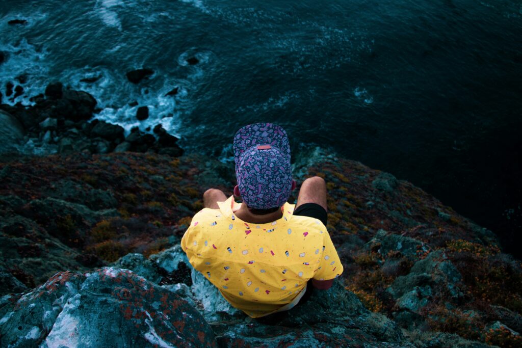 Man wearing a unique patterned outfit, sat over a cliff edge. 