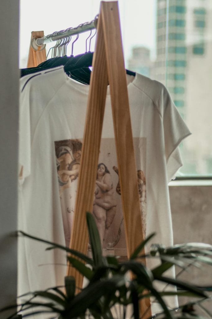 White t-shirt with artistic print displayed on wooden clothing stand.