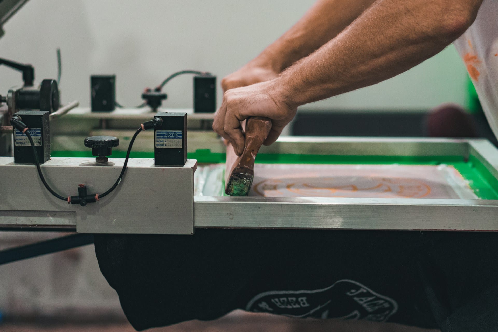Person using screen printing equipment to create custom t-shirt design.