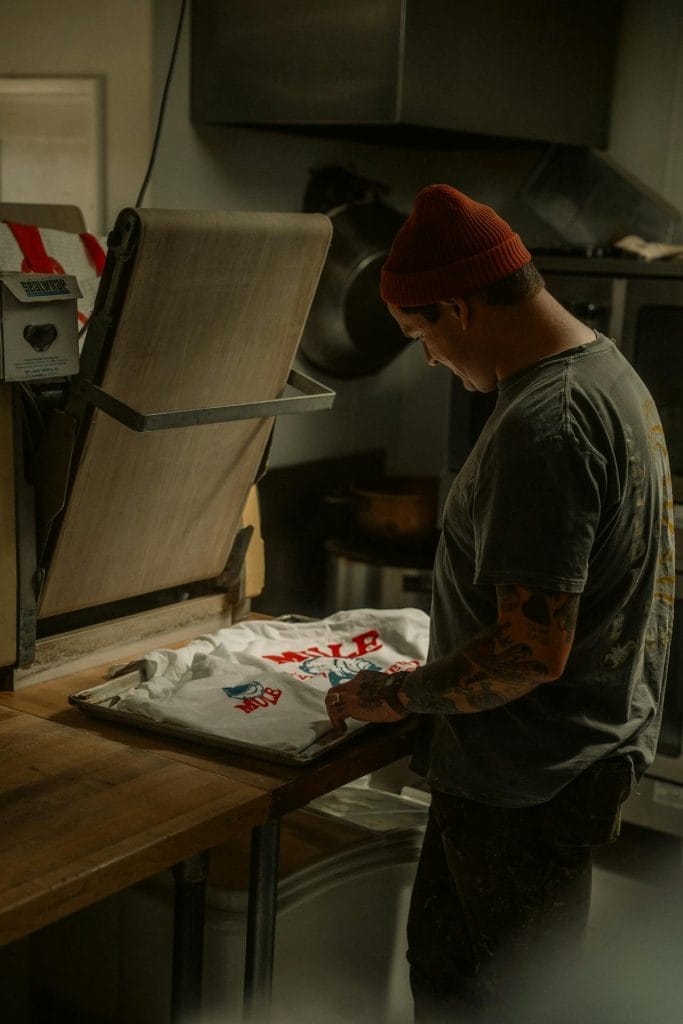 Man heat pressing custom design onto white t-shirt in workshop.